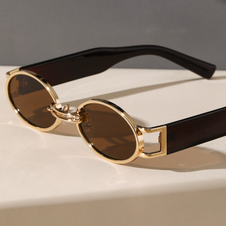 Round sunglasses with a durable metal frame, gold accents, and dark brown lenses rest on a light surface. Black arms and a unique geometric hinge design add flair, while UV400 protection ensures your eyes stay safe in bright lighting.