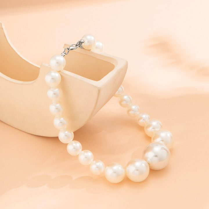 A string of glossy white pearls from a pearl jewelry set is draped over the edge of a beige, minimalist ceramic bowl on a soft peach background, creating an elegant and serene display.