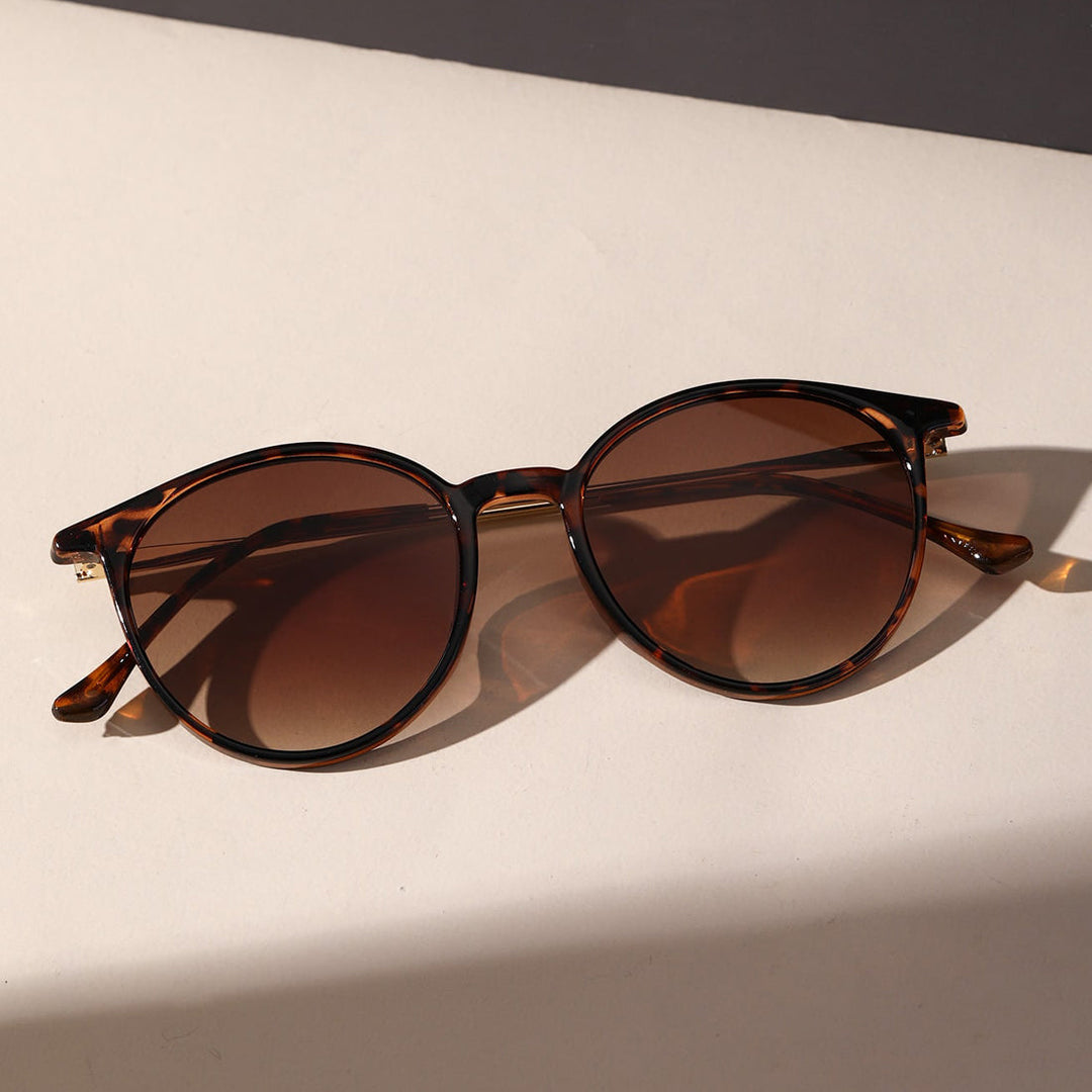 Tortoiseshell round sunglasses with brown tinted lenses offer UV protection, resting on a light-colored surface and casting a faint shadow.