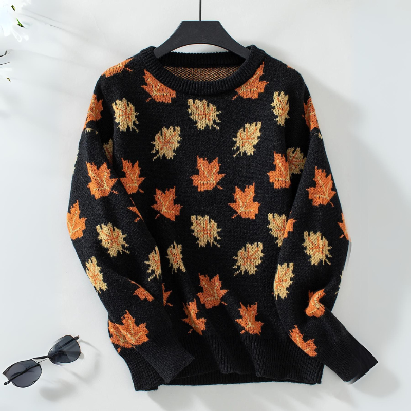 A comfortable sweater made from soft knit material, decorated with an all-over orange and yellow maple leaf pattern, is displayed on a hanger against a white background, with a pair of sunglasses placed nearby.