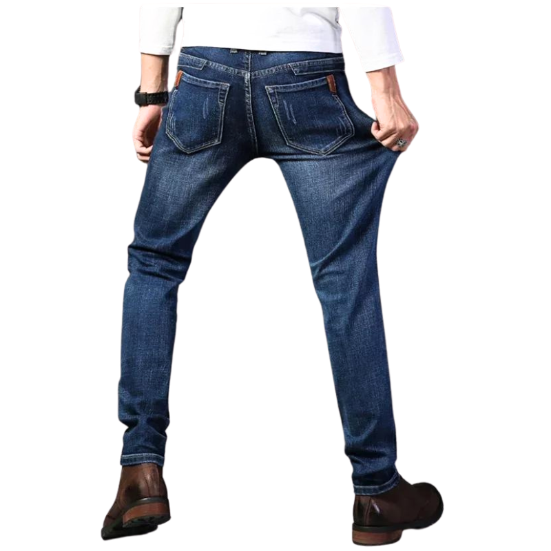 A person wearing slim-fit jeans made from stretch denim, brown shoes, and a white long-sleeve shirt is shown from the back, pulling the sides of the jeans to demonstrate their stretchiness.
