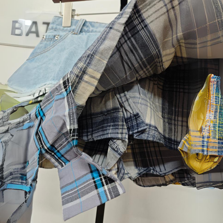 A close-up of denim and plaid garments hanging on a rack, featuring an eclectic fashion vibe with a clear plastic yellow bag and a partially visible BATZ sign in the background.