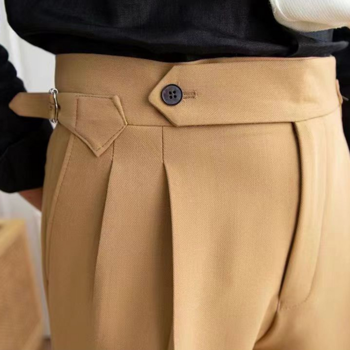 Close-up of a person wearing high-waisted, tan pleated pants with a tailored fit and side buckle detail, styled with a black top tucked in for an old money aesthetic.