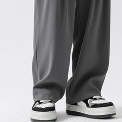 A person wearing wide-leg gray streetwear joggers and black-and-white sneakers stands on a white surface.