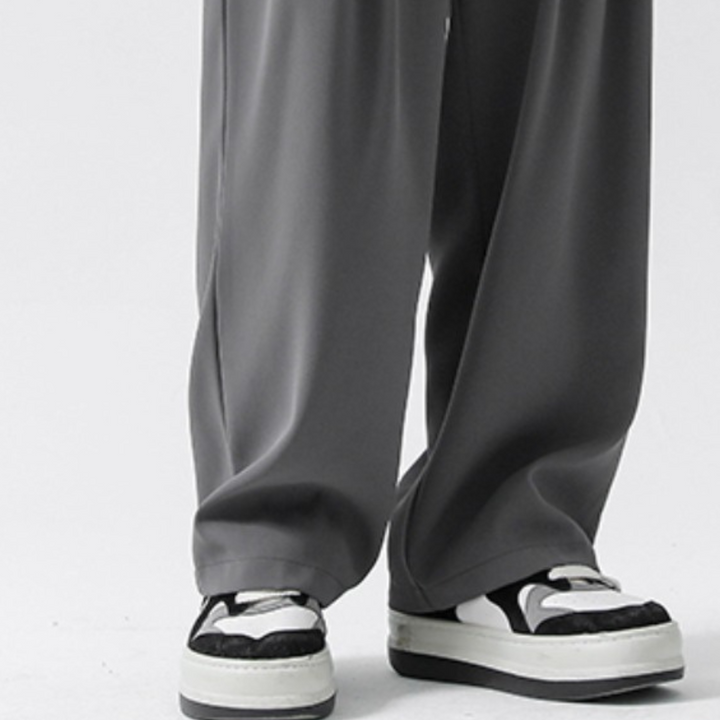 A person wearing wide-leg gray streetwear joggers and black-and-white sneakers stands on a white surface.