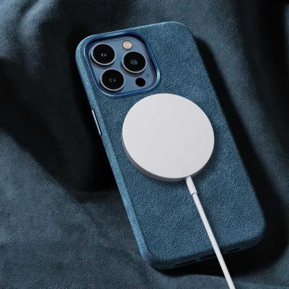 A smartphone with a blue case featuring a suede finish is lying on a matching blue fabric surface, with a white MagSafe wireless charger attached to its back.