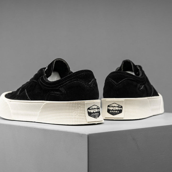 A pair of black suede lace-up sneakers with thick white soles and a JIAMEI label on the heel, featuring comfortable cushioning, displayed on a gray platform against a plain gray background.