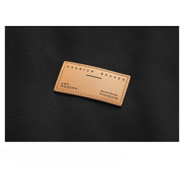 A tan leather patch with PREMIUM BRANDS, ART MODERN, and Premium Goods Finest Quality embossed, sewn onto a black fabric background, perfectly complements this windproof jacket with adjustable cuffs.