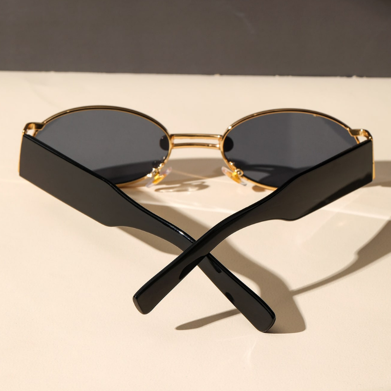 A pair of retro oval sunglasses with a durable metal frame, gold rims, and dark UV400 protection lenses sits on a light surface, with the black arms crossed in an X shape in the foreground.