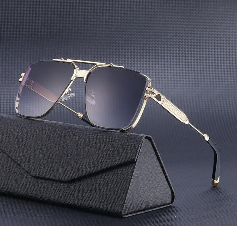 A pair of gold-framed vintage aviator sunglasses with dark gradient lenses and UV400 protection rests on a black, textured eyeglass case against a dark grey, patterned background.
