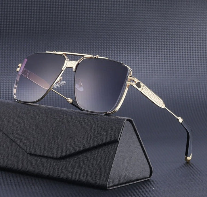 A pair of gold-framed vintage aviator sunglasses with dark gradient lenses and UV400 protection rests on a black, textured eyeglass case against a dark grey, patterned background.