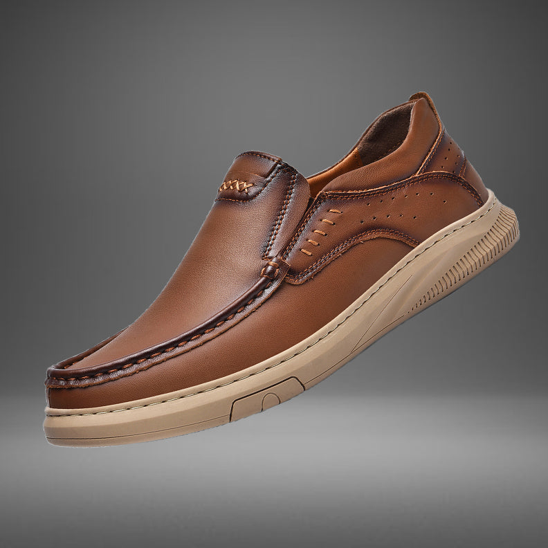 A brown men's cowhide leather slip-on shoe with visible stitching and a beige soft sole, displayed against a gradient gray background.