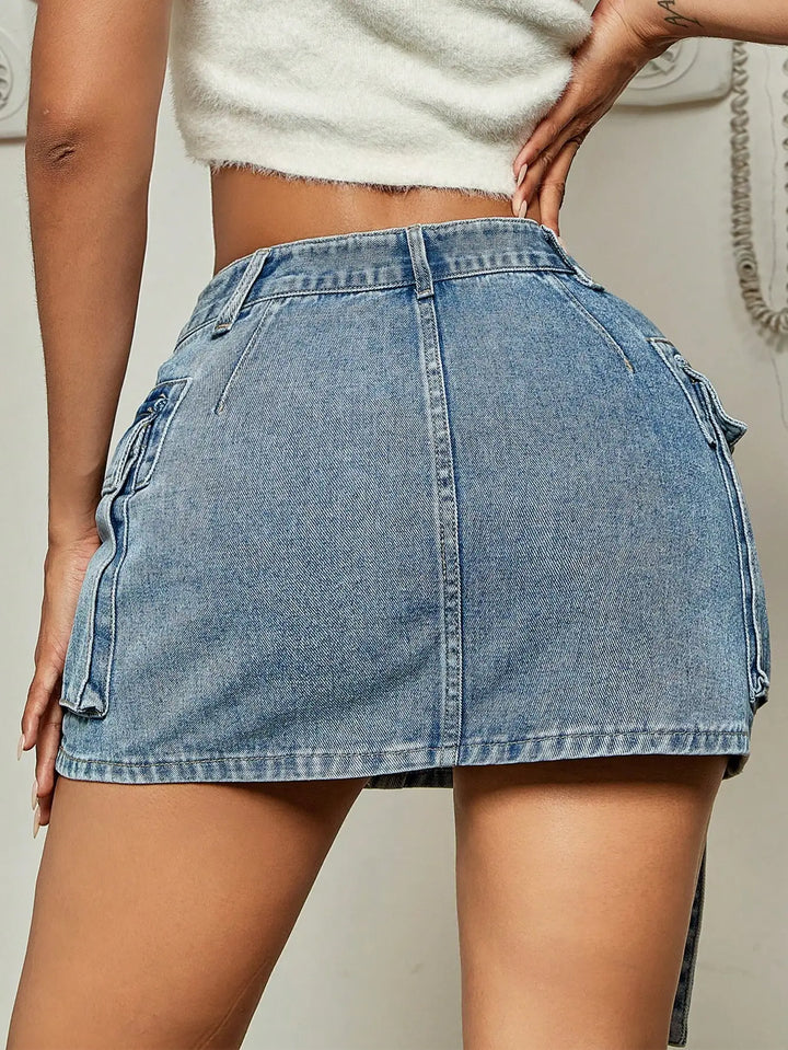 A person wearing a high-waisted, light blue denim mini skirt with flap pockets and a white cropped top, embodying street tooling style as they stand with their back to the camera.