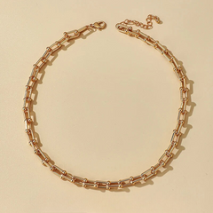 A gold-toned statement chain necklace with rectangular links and small round connectors is laid out in a circular shape on a beige background, crafted from durable 316L stainless steel.