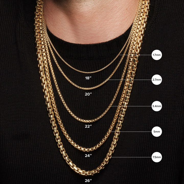 A person wearing six collectable jewelry chains of varying thicknesses and lengths—1.7mm/18, 2.7mm/20, 3.4mm/22, 5mm/24, and 7.5mm/26—over a black sweater, each adorned with a gold plated amulet for added flair.