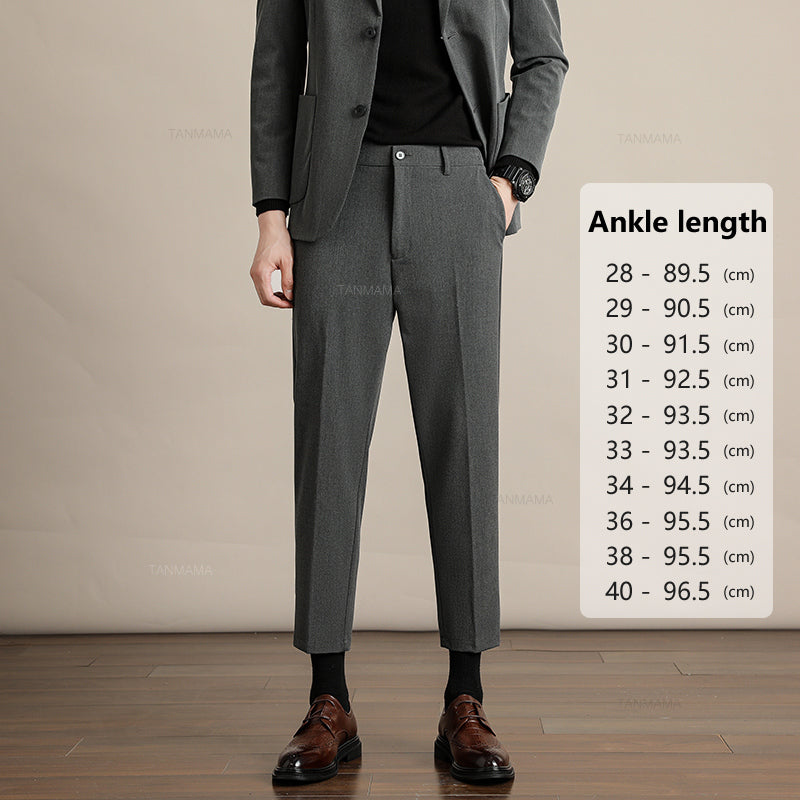 A person in business formal attire—a dark grey suit, black shirt, and brown dress shoes—stands on a wooden floor. A chart beside them lists mens slim casual trousers ankle length in centimeters for waist sizes 28 to 40.