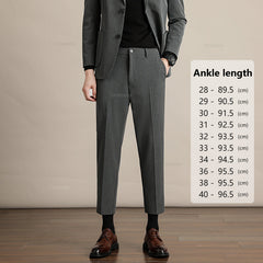 A person in business formal attire—a dark grey suit, black shirt, and brown dress shoes—stands on a wooden floor. A chart beside them lists mens slim casual trousers ankle length in centimeters for waist sizes 28 to 40.