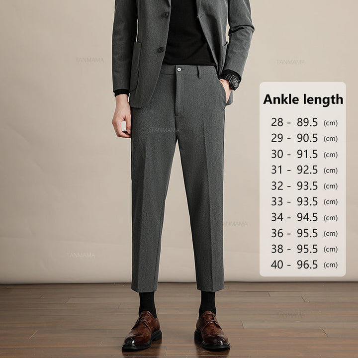 A person in business formal attire—a dark grey suit, black shirt, and brown dress shoes—stands on a wooden floor. A chart beside them lists mens slim casual trousers ankle length in centimeters for waist sizes 28 to 40.