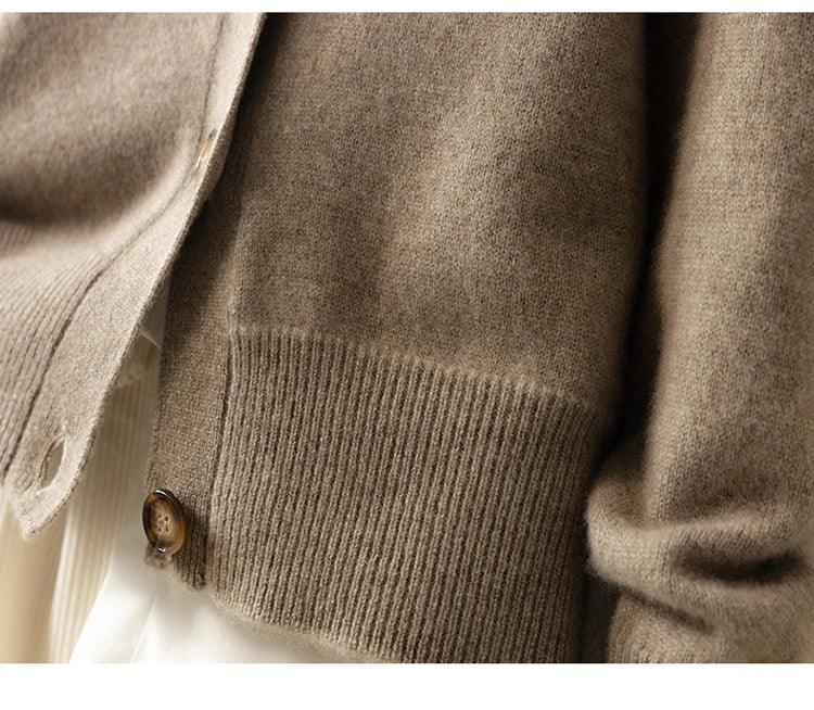 Close-up of an ultra soft cashmere cardigan, highlighting a ribbed hem and button detail. The 100% wool cashmere fabric appears cozy, with part of a cream-colored garment visible underneath.