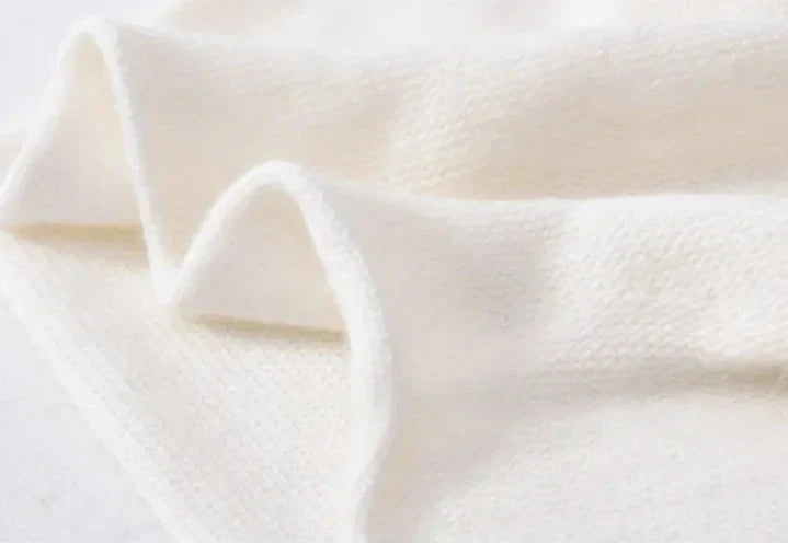 A close-up of soft, white cashmere fabric with a slightly fuzzy texture, gently folded to show its thickness and smooth surface.