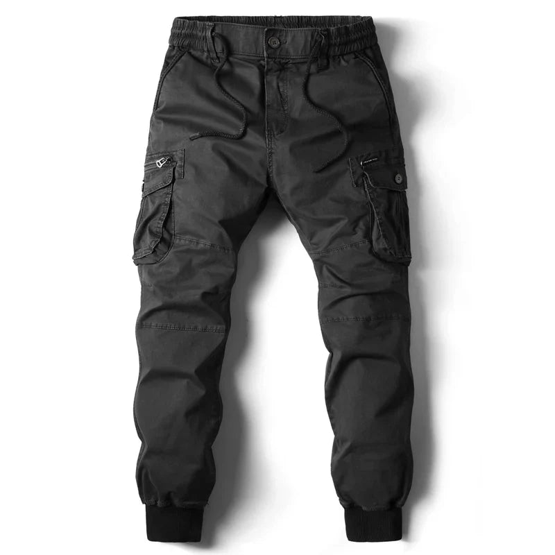 Black cargo jogger pants featuring street style flair with an elastic waistband and drawstring, multiple cargo pockets including zippered and flap options, plus ribbed cuffs at the ankles, laid flat on a white background.
