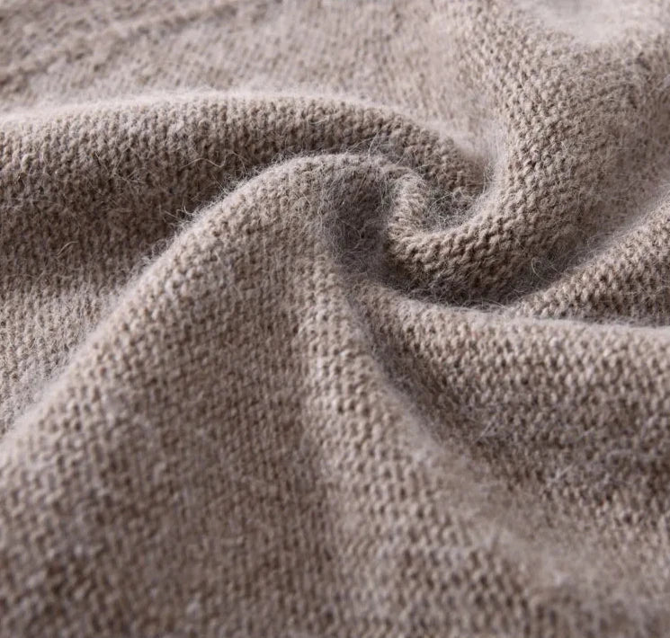 Close-up of a soft, beige cashmere knitted fabric with a visible swirl fold, showing the lightweight texture and fine fibers of the material.