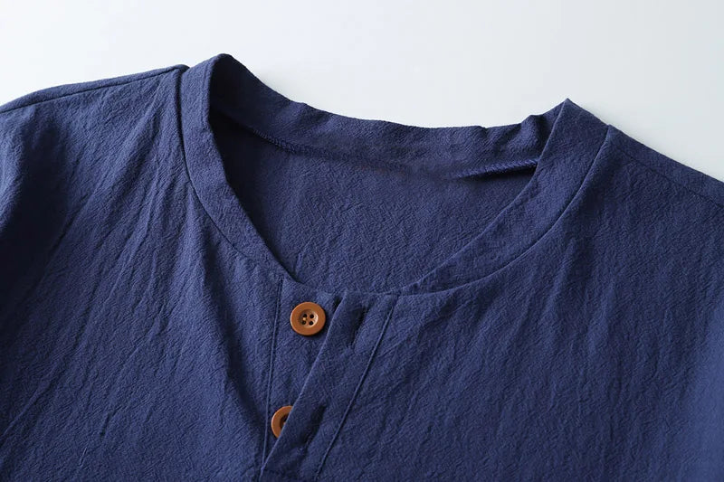A close-up of the collar and upper part of a navy blue Japanese linen shirt with a round neckline and two brown buttons, showcasing the breathable, lightweight summer shirt on a white background.