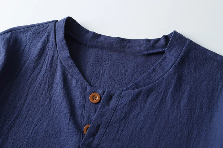 A close-up of the collar and upper part of a navy blue Japanese linen shirt with a round neckline and two brown buttons, showcasing the breathable, lightweight summer shirt on a white background.