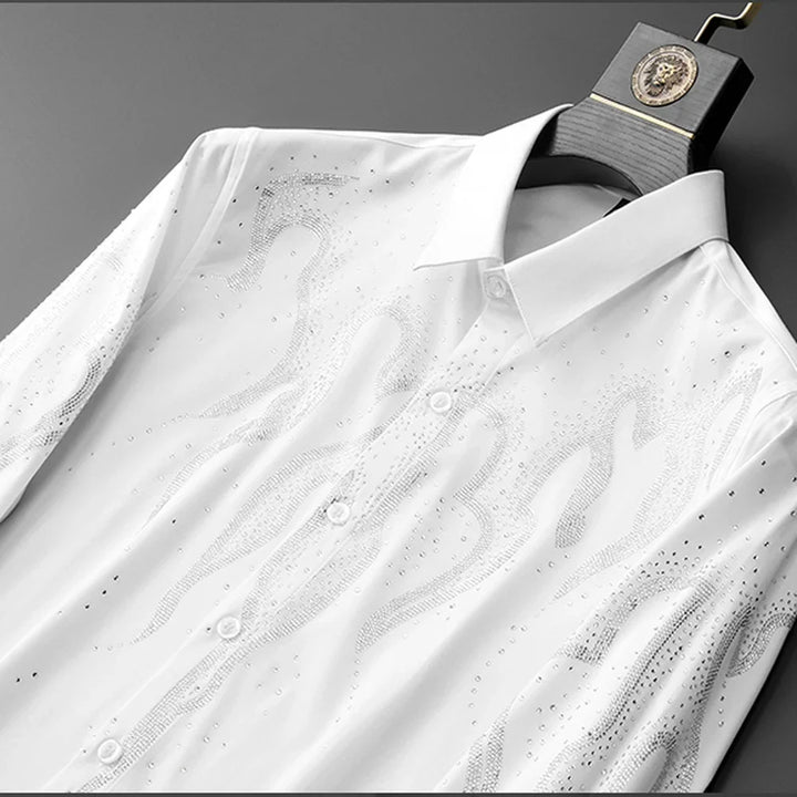 A tailored fit rhinestone shirt, this white button-up features a subtle flame pattern made of small, shiny rhinestones, displayed on a black hanger with a decorative gold emblem.
