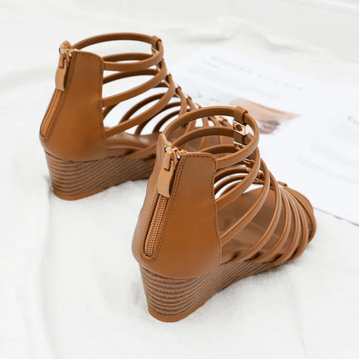 A pair of tan wedge sandals with multiple thin straps and back zippers, displayed on a white surface with some papers in the background—an elegant addition to any women shoes collection.