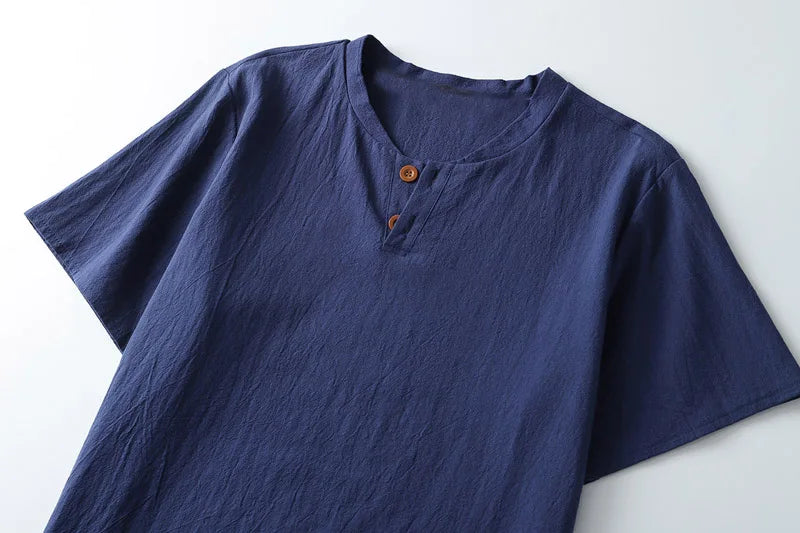 A dark blue, lightweight summer shirt with short sleeves, a round, slightly open neckline, and two brown buttons at the collar, laid flat on a white surface.