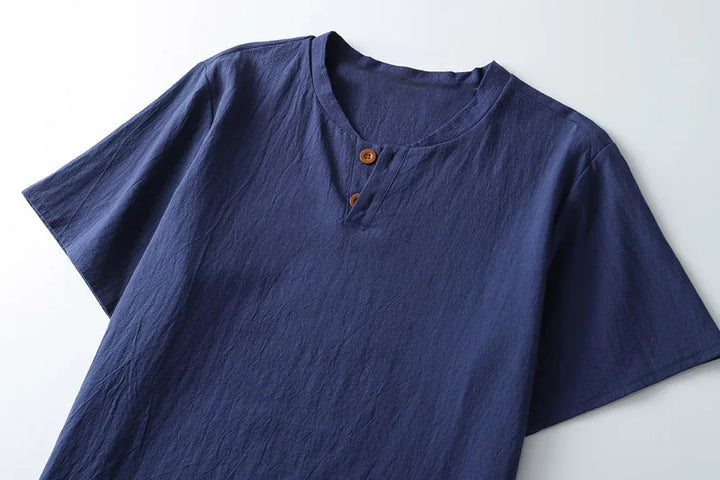 A dark blue, lightweight summer shirt with short sleeves, a round, slightly open neckline, and two brown buttons at the collar, laid flat on a white surface.
