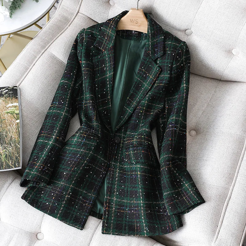 A green and black plaid blazer with subtle yellow and red lines, perfect as a Stylish Jacket Coat for office work, is displayed on a hanger atop a light beige tufted sofa. The interior lining of this formal blazer is dark green.