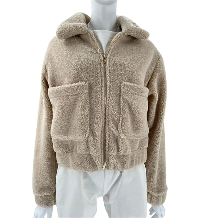 A mannequin wears a beige, zip-up sherpa fur fleece jacket with a hood and two large front pockets, paired with white pants—perfect for all season style.