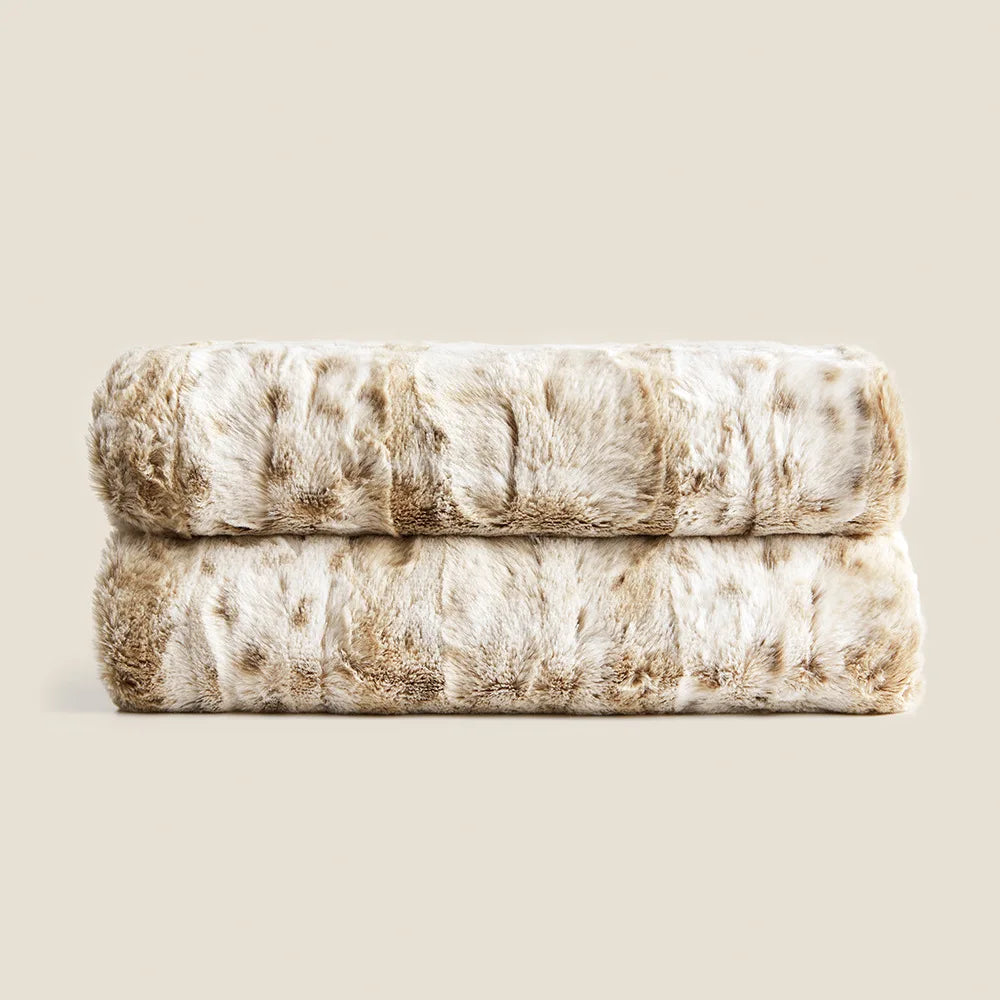 A folded ultra-soft luxurious blanket in shades of beige and light brown sits against a neutral background, showcasing its plush and soft texture.