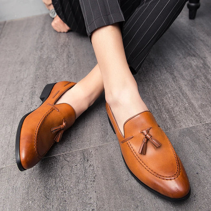 A persons legs and feet wearing brown mens loafers crafted from genuine leather.