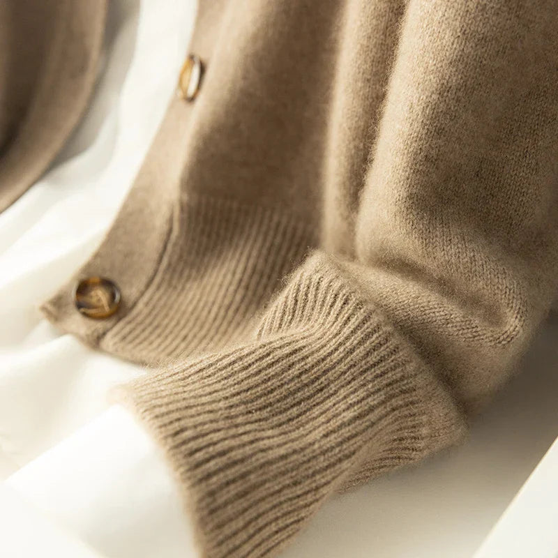 Close-up of a light brown ultra soft cashmere cardigan sleeve and buttons, laid over a white surface. The soft texture and ribbed cuff detail are visible, highlighting the cozy 100% wool cashmere fabric.