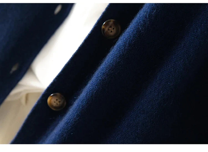 Close-up of an ultra soft navy blue 100% wool cashmere cardigan, featuring two dark brown buttons and part of a white garment visible underneath.