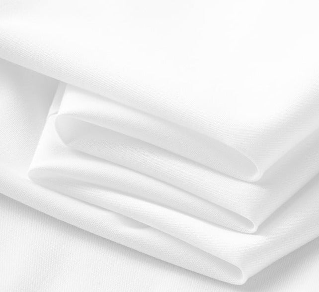 A close-up view of several layers of smooth, neatly folded white fabric, showcasing the clean and soft texture typical of a classic button-up shirt.