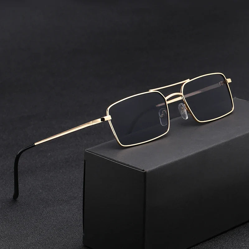 Rectangular sunglasses with thin gold, lightweight alloy frames and black lenses offer UV400 protection, displayed on a black box against a dark background.