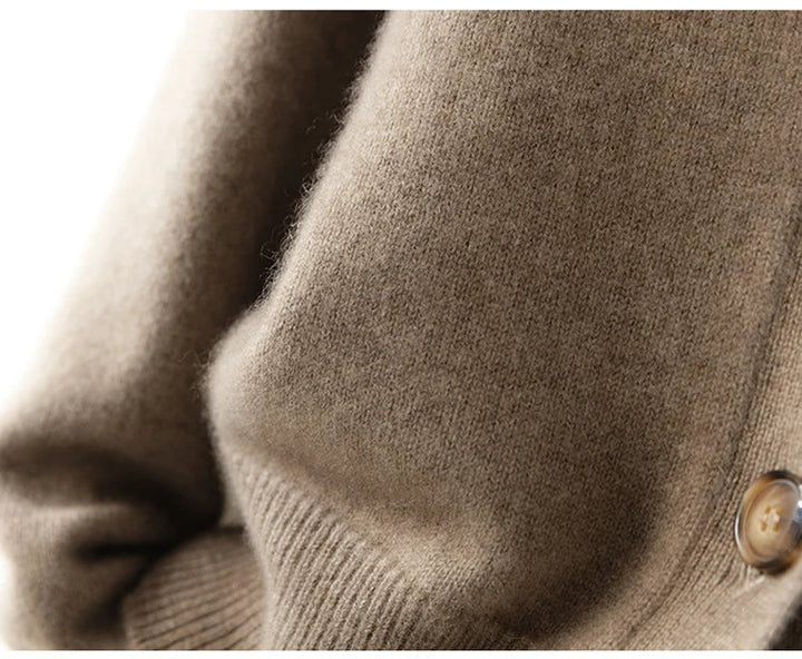 Close-up of an ultra soft, light brown cashmere cardigan sleeve, featuring a ribbed cuff and tan button on the side. The 100% wool cashmere texture appears smooth and cozy.