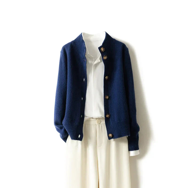 An ultra soft navy blue cashmere cardigan layered over a white collared shirt, paired with high-waisted cream-colored trousers, displayed against a plain white background.
