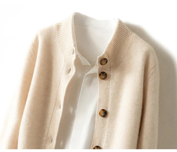 A close-up of an ultra soft, cream-colored cashmere cardigan with brown buttons layered over a white collared shirt, displayed against a white background.