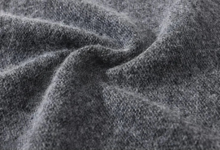 Close-up of soft, textured gray wool fabric with visible fibers and gentle folds, evoking the cozy feel of a lightweight slouchy beanie.