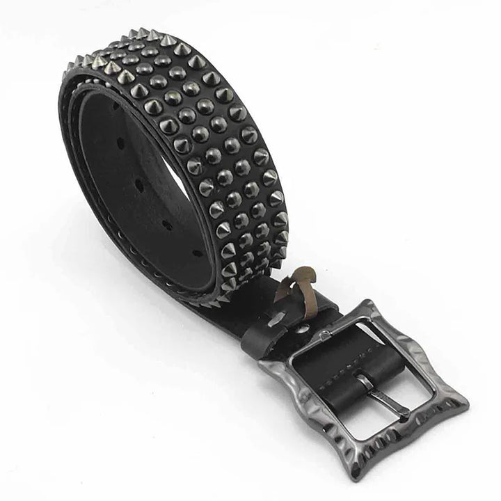 A rolled-up black leather belt featuring multiple rows of metal spikes, studded detailing, and a metal buckle with a hammered texture.