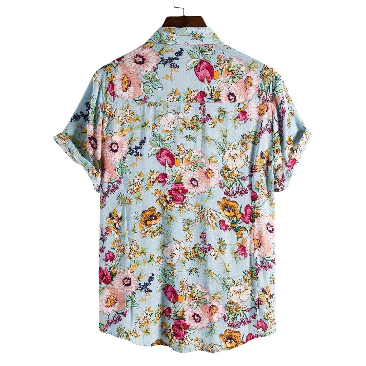 A vintage-inspired shirt, this light blue, short-sleeve button-up features a colorful floral pattern in pink, yellow, purple, and green. The lightweight linen shirt is shown on a hanger with the back facing forward.