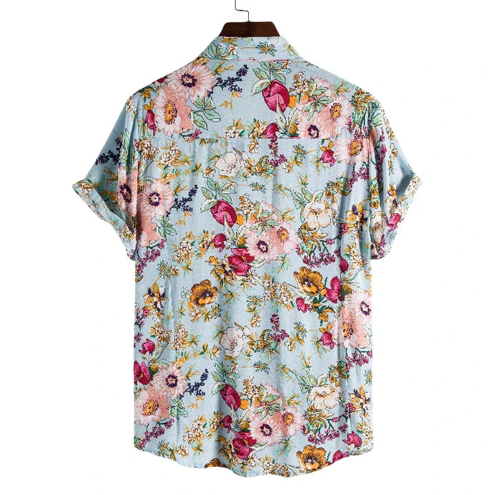 A vintage-inspired shirt, this light blue, short-sleeve button-up features a colorful floral pattern in pink, yellow, purple, and green. The lightweight linen shirt is shown on a hanger with the back facing forward.