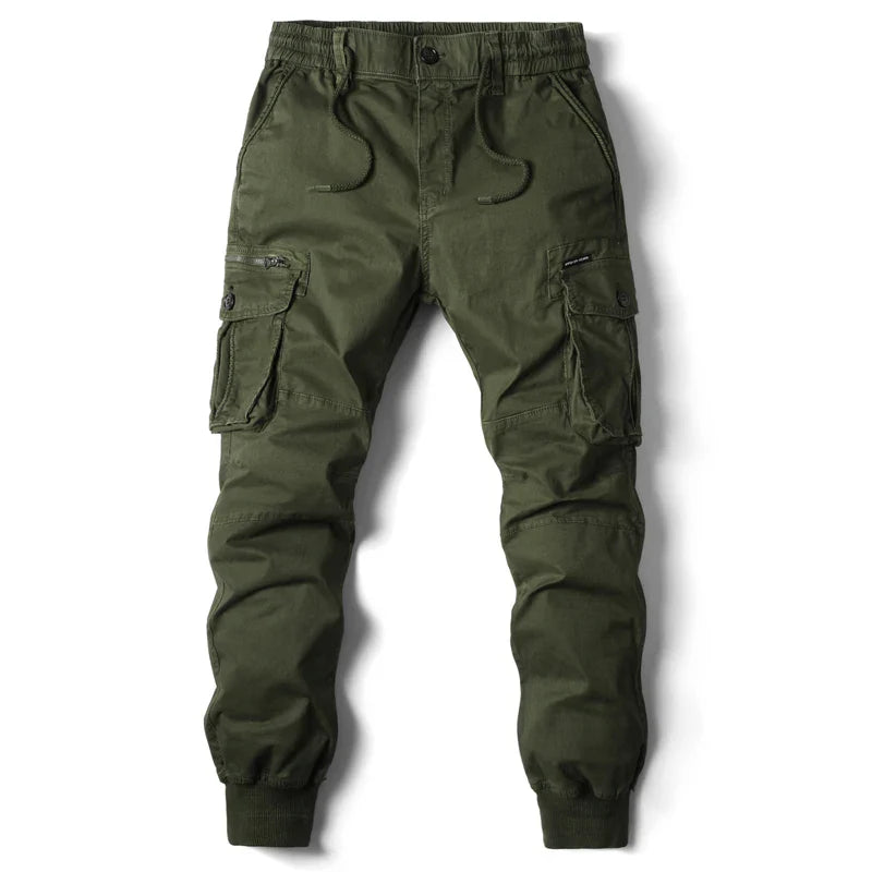 Olive green cargo jogger pants with an elastic waistband, drawstring, multiple cargo pockets including two large side pockets with flaps, zipper details, and elastic cuffs at the ankles. Perfect for street style or tactical pants-inspired looks. Laid flat on white background.