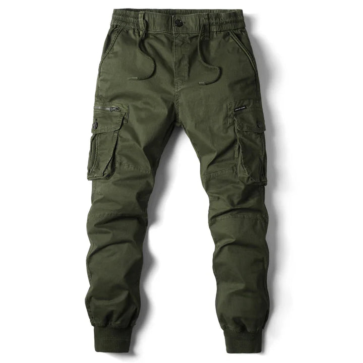 Olive green cargo jogger pants with an elastic waistband, drawstring, multiple cargo pockets including two large side pockets with flaps, zipper details, and elastic cuffs at the ankles. Perfect for street style or tactical pants-inspired looks. Laid flat on white background.