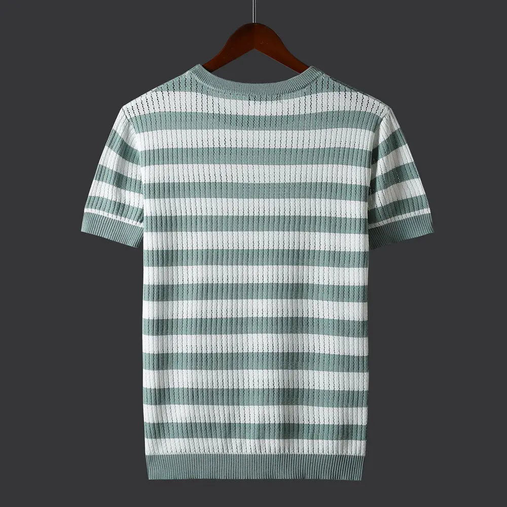 A short-sleeve, light green and white horizontal striped knit shirt with a comfort-fit design is displayed on a brown wooden hanger against a dark gray background. The back of the shirt is visible.